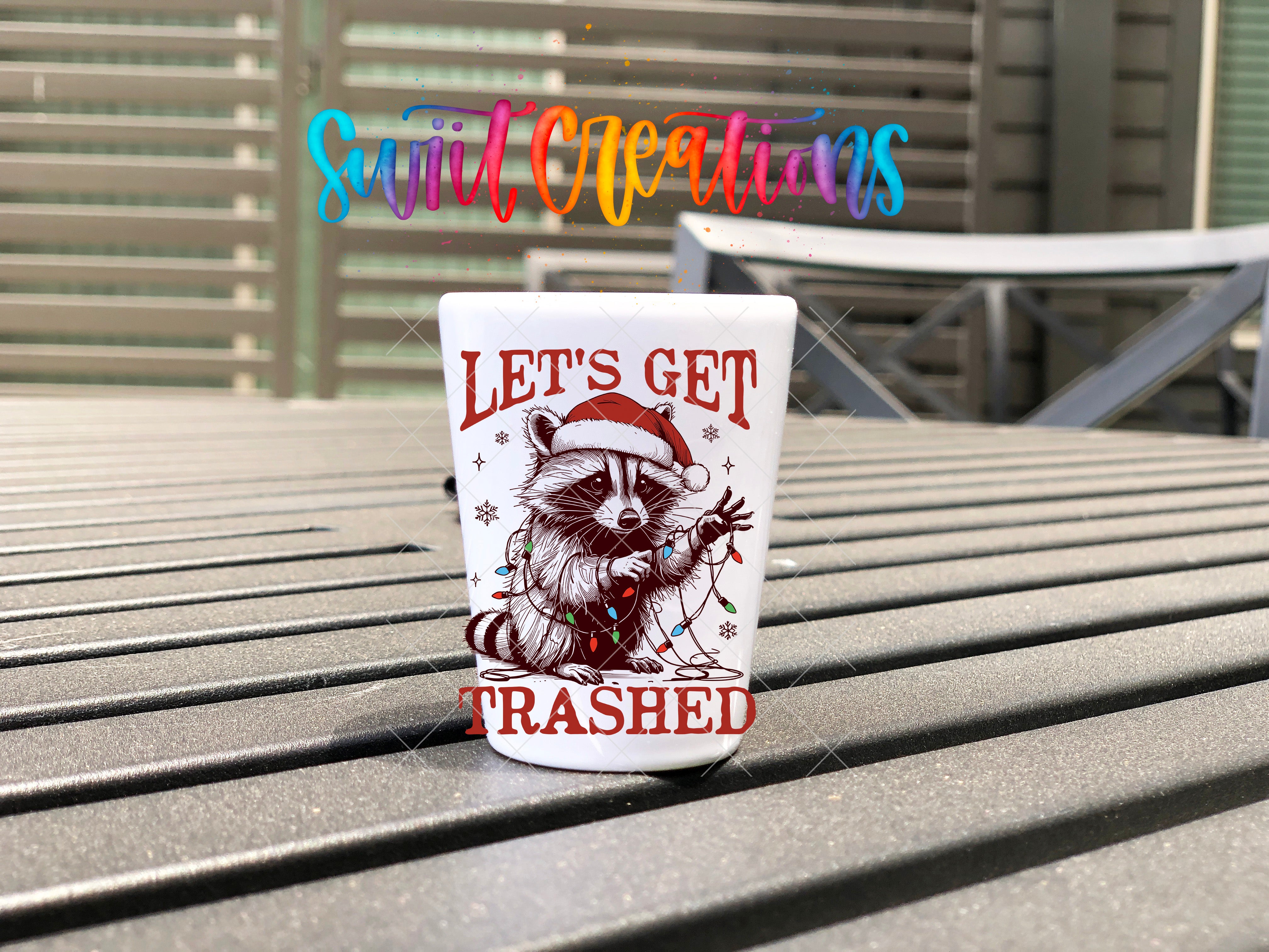 A white mug with a raccoon wearing a Santa hat and the text "Let's get trampled" printed on it, placed on a wooden surface.