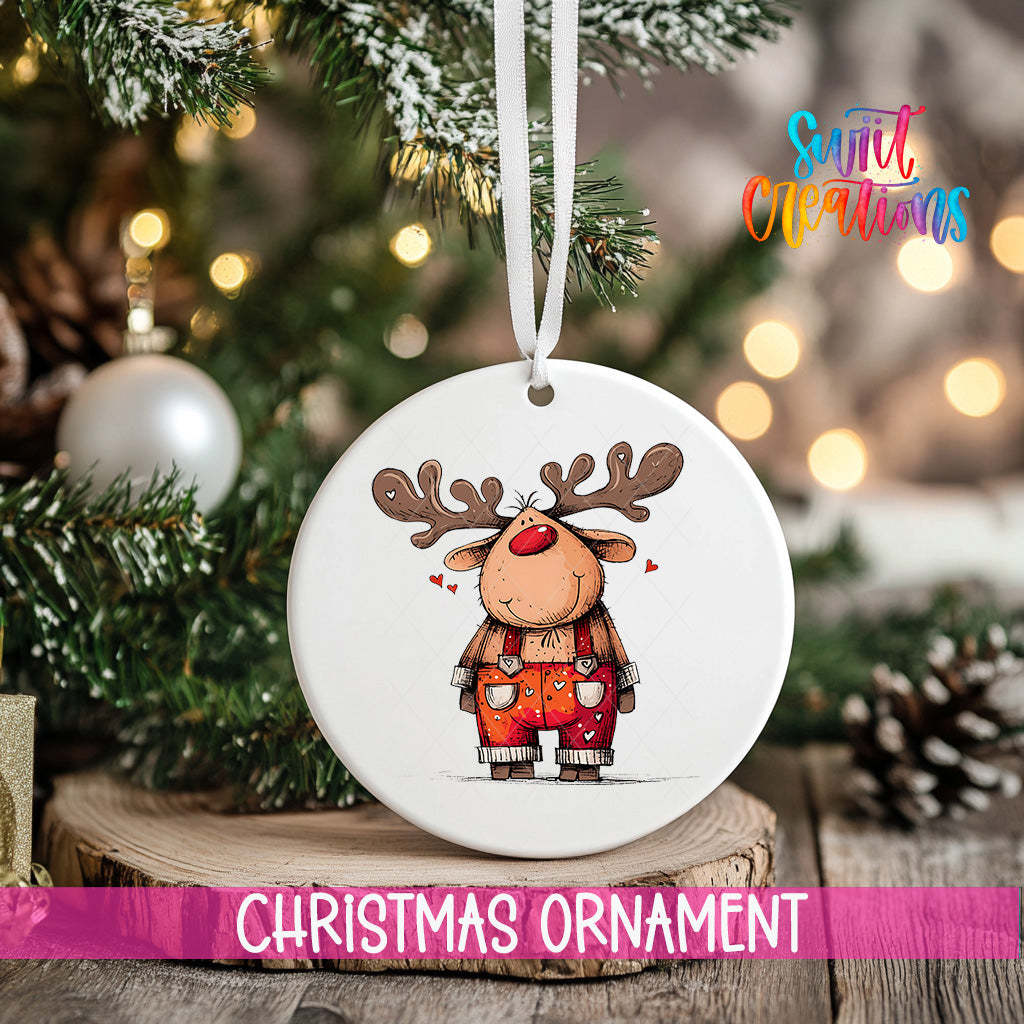 A white Christmas ornament featuring a cartoon reindeer with antlers and a red nose, hanging on a tree branch.