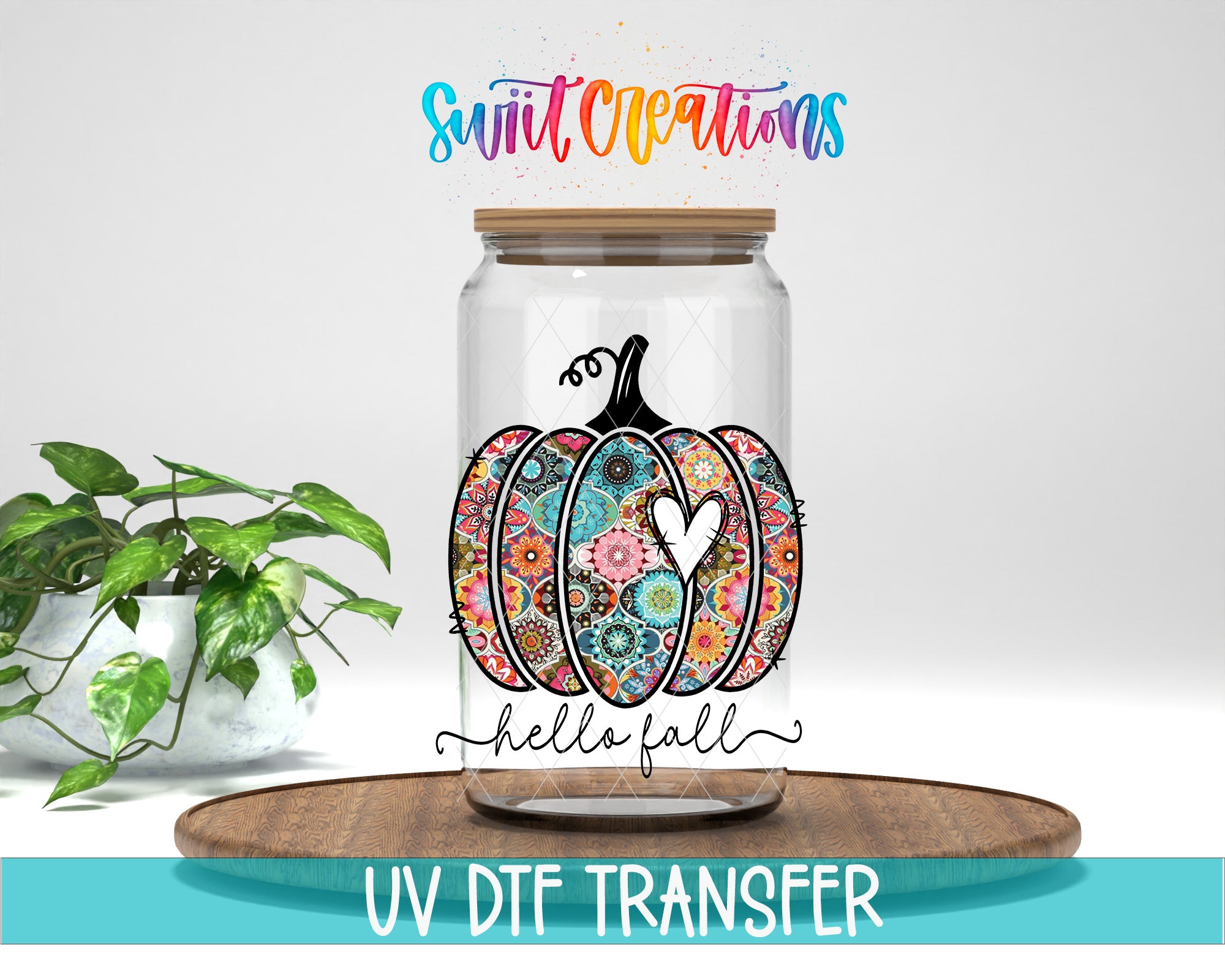 a glass jar with a pumpkin design and the text "Hello fall" on it, placed on a wooden surface. There is also a plant in the background.