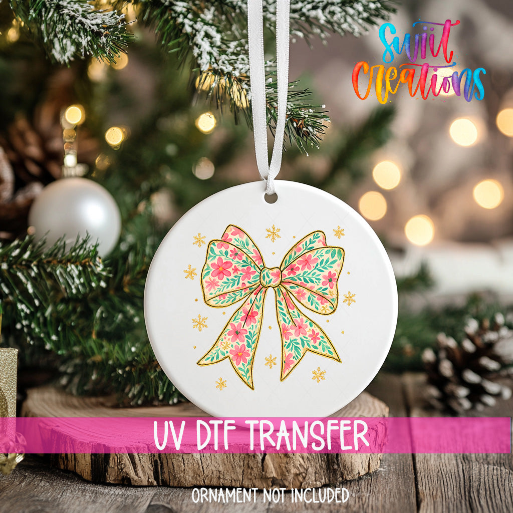 A white ceramic ornament with a floral design and a bow is hanging on a Christmas tree.