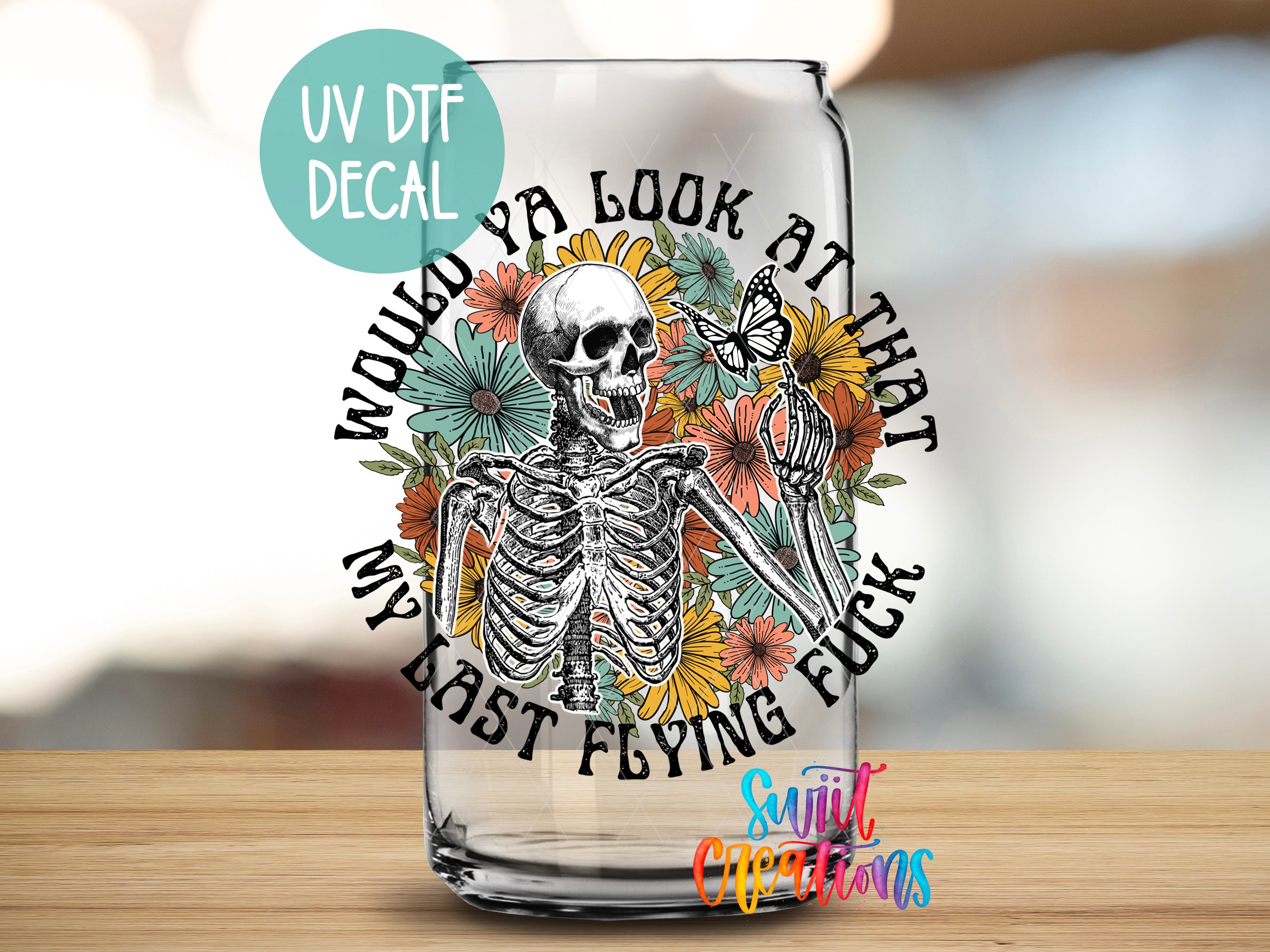A glass with a skeleton and floral design, along with the text "UV DTF DECAL" and "WOULD ya look at that MY LAST FLYING FUCK" printed on it.