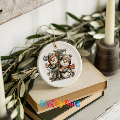 A ceramic ornament featuring two snowmen is placed on top of a stack of books, surrounded by greenery.