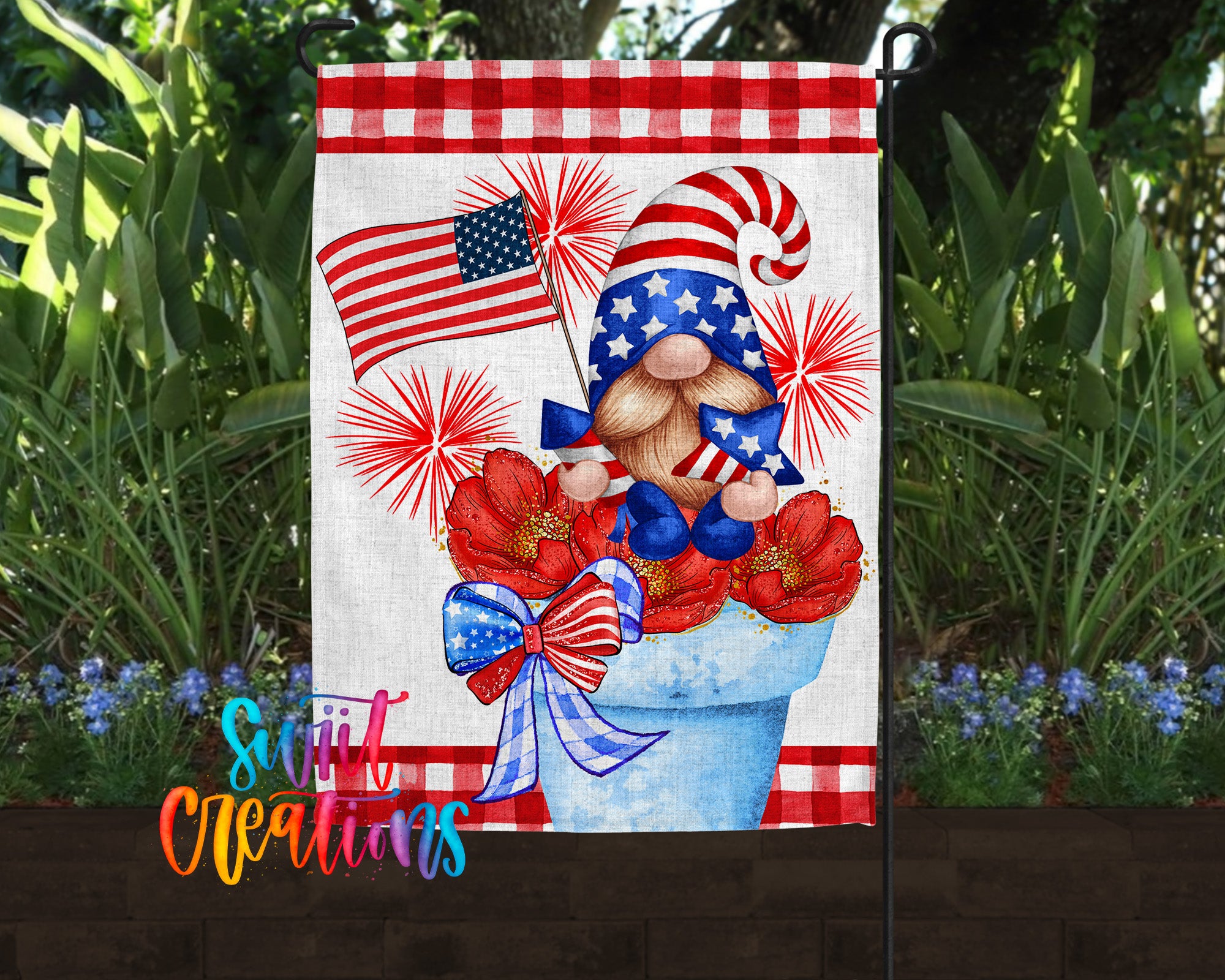 A patriotic-themed garden flag featuring a gnome holding an American flag and surrounded by red and white flowers, with a fireworks display in the background.