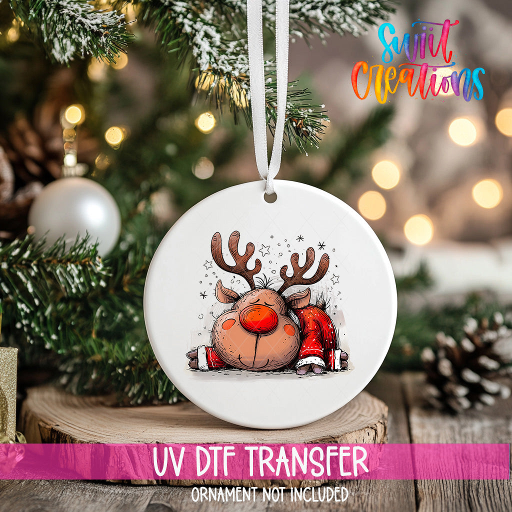 A white ornament with a cartoon reindeer design hangs on a Christmas tree, surrounded by pine branches and twinkling lights.