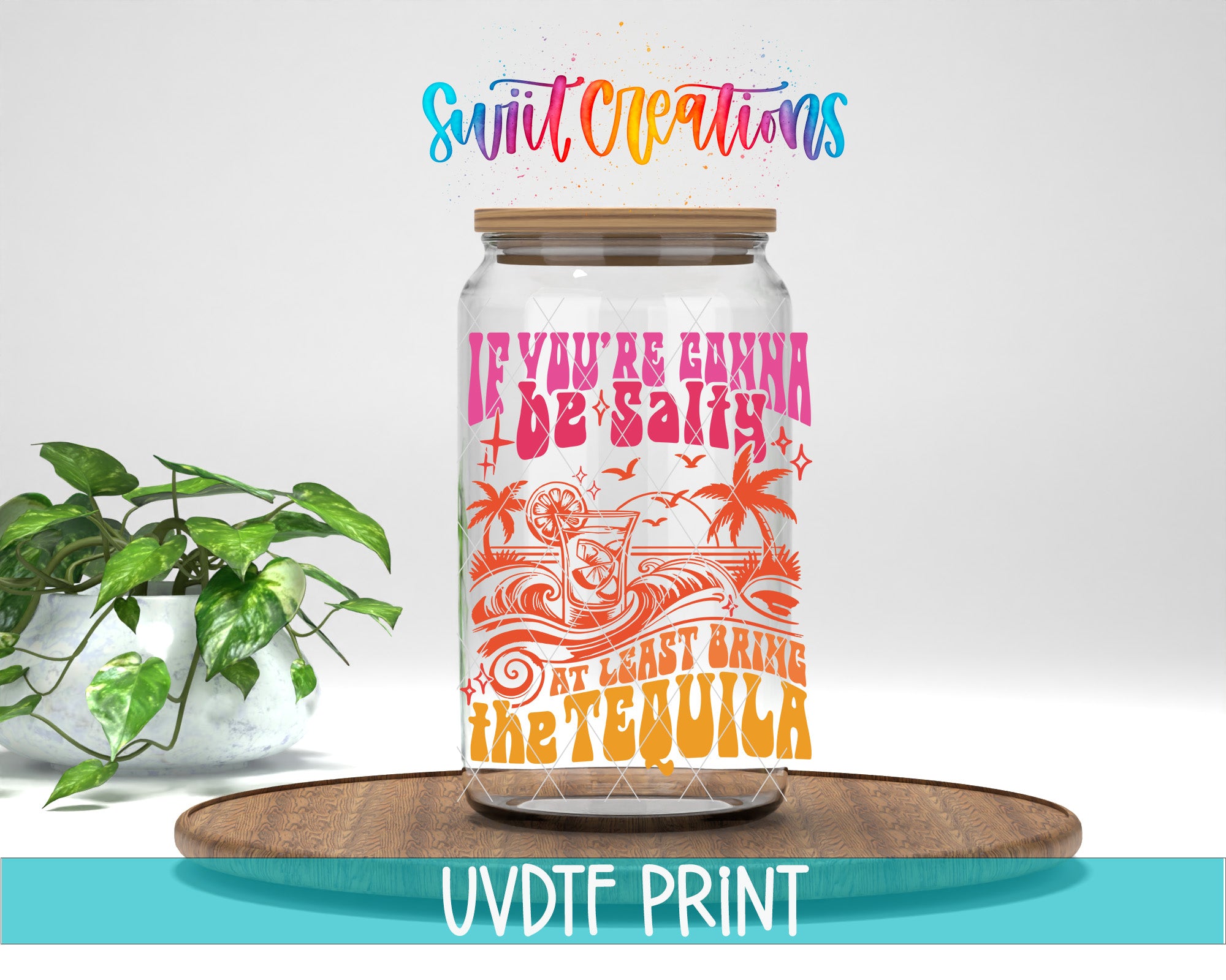 A colorful glass jar with a label that says "If you're gonna be salty, at least bring the tequila" is displayed on a wooden surface, with a potted plant in the background.