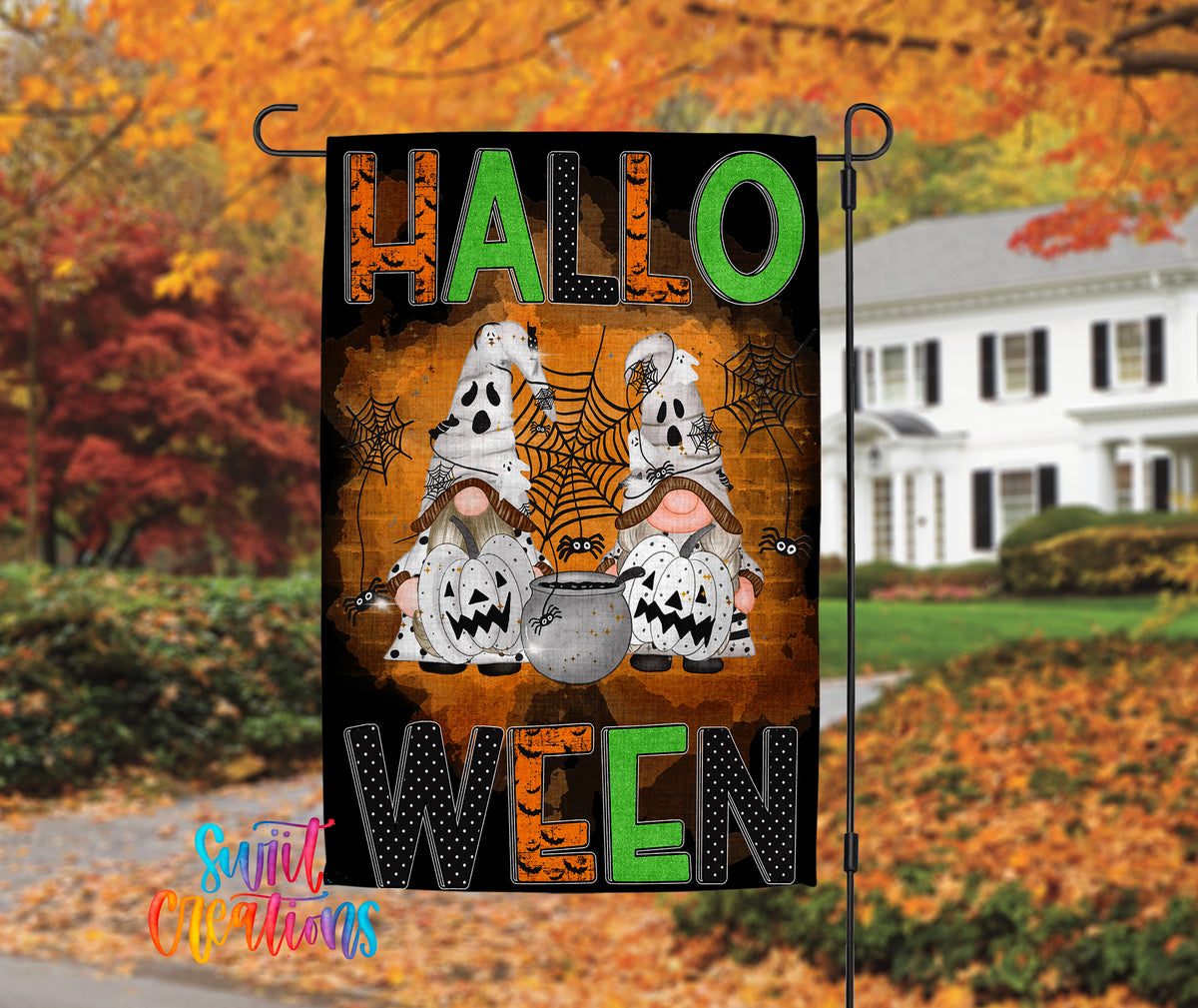 A Halloween-themed garden flag with two ghostly gnomes and a spider web, set against a backdrop of autumn foliage.