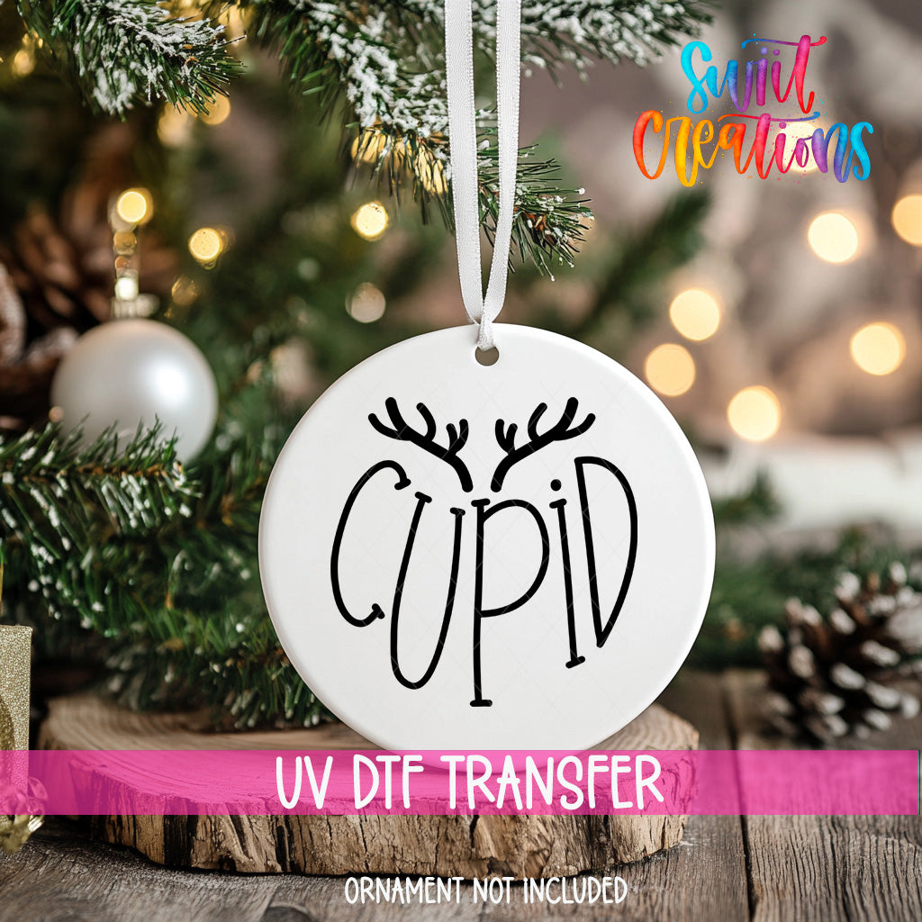 A white ornament with the word "CUPID" written on it, hanging on a Christmas tree.