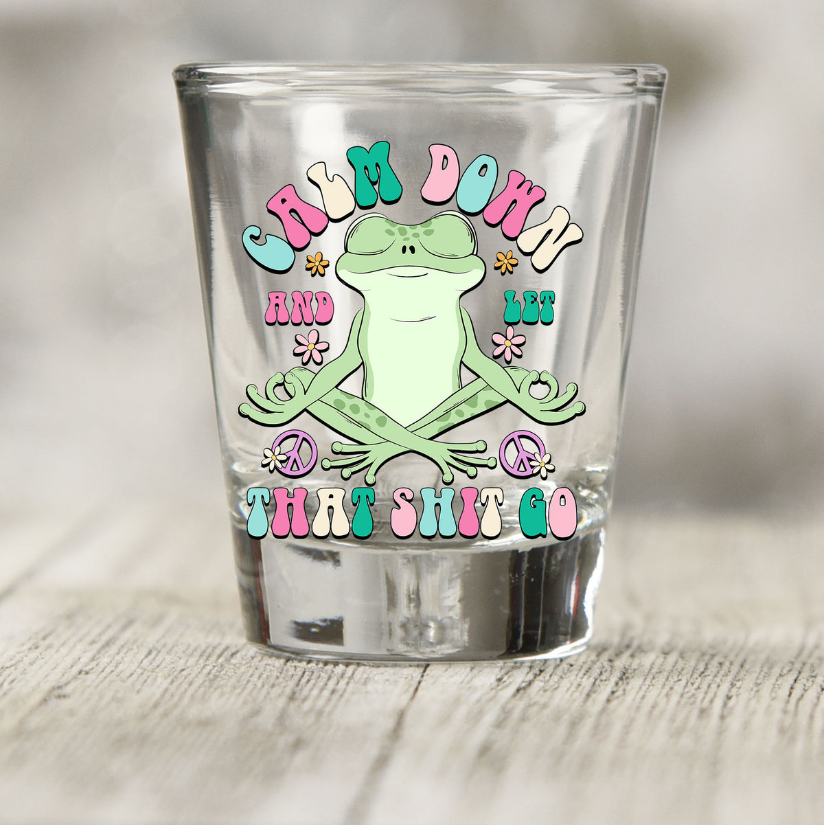 Calm Down And Let That Sh*t Go shot glass UV DTF transfer with meditating frog with flowers and peace signs on a clear shot glass