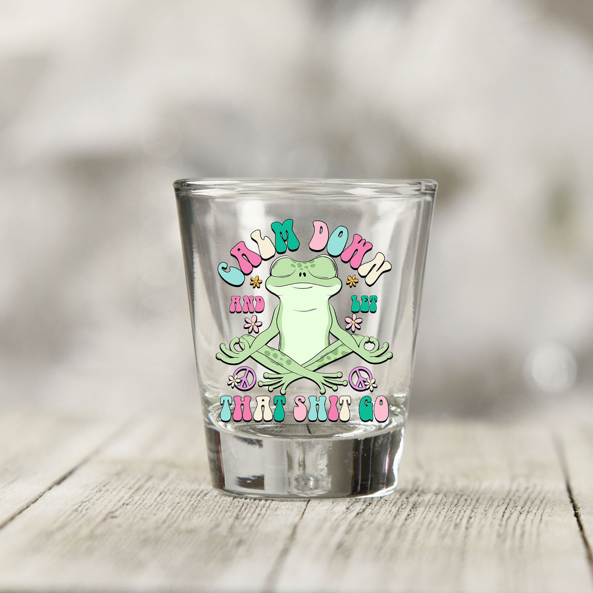 Close-up of the Calm Down And Let That Sh*t Go UV DTF transfer on a clear shot glass