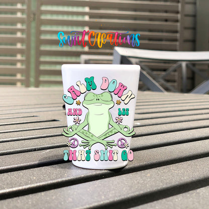 Calm Down And Let That Sh*t Go UV DTF transfer on a white shot glass on an outdoor patio table