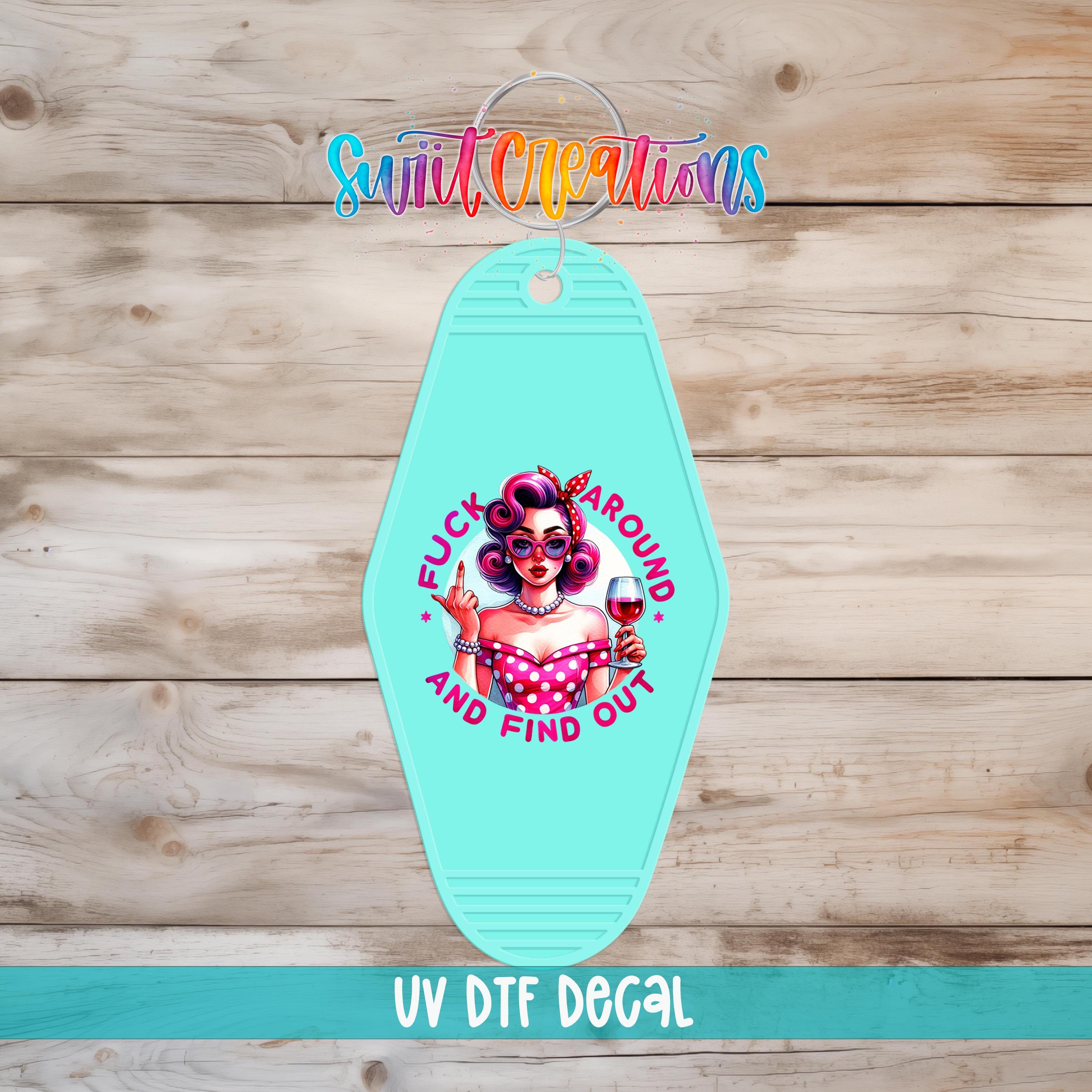 A turquoise keychain with a colorful graphic design featuring a woman with curly hair and a pink dress, along with the text "FUCK AROUND AND FIND OUT" and "UV Dtf Decal".