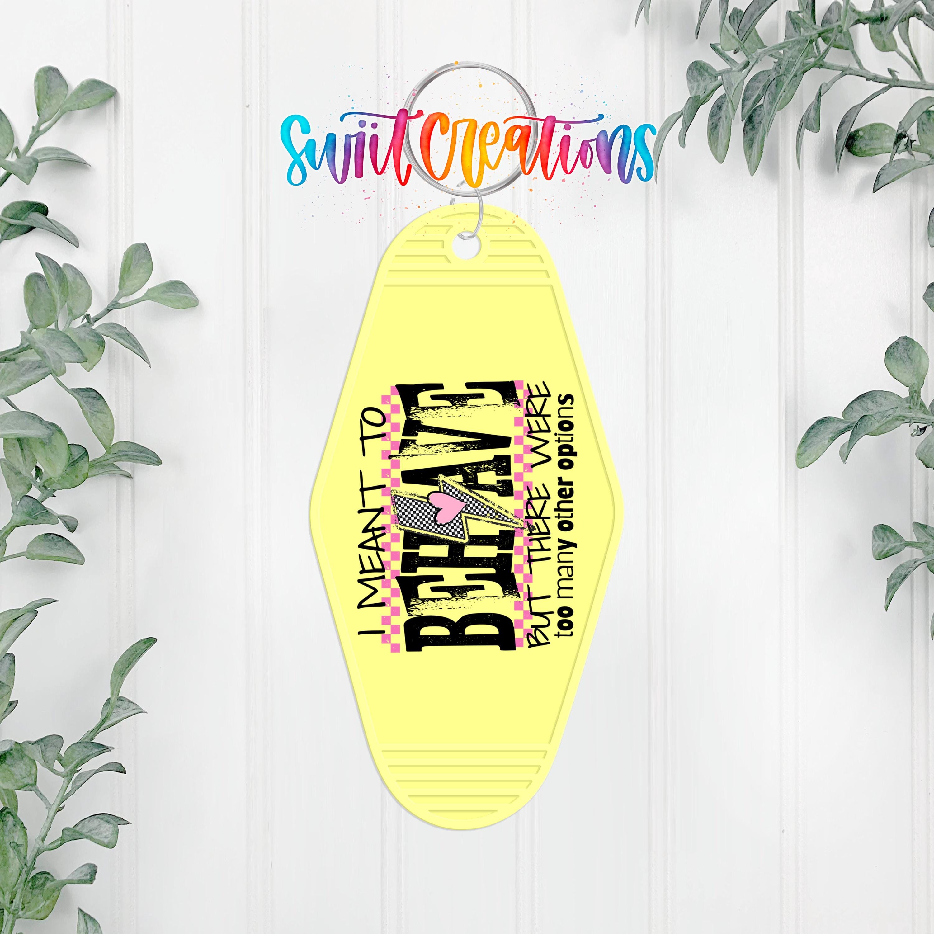 A yellow keychain with a colorful design hangs on a white wall, surrounded by greenery.