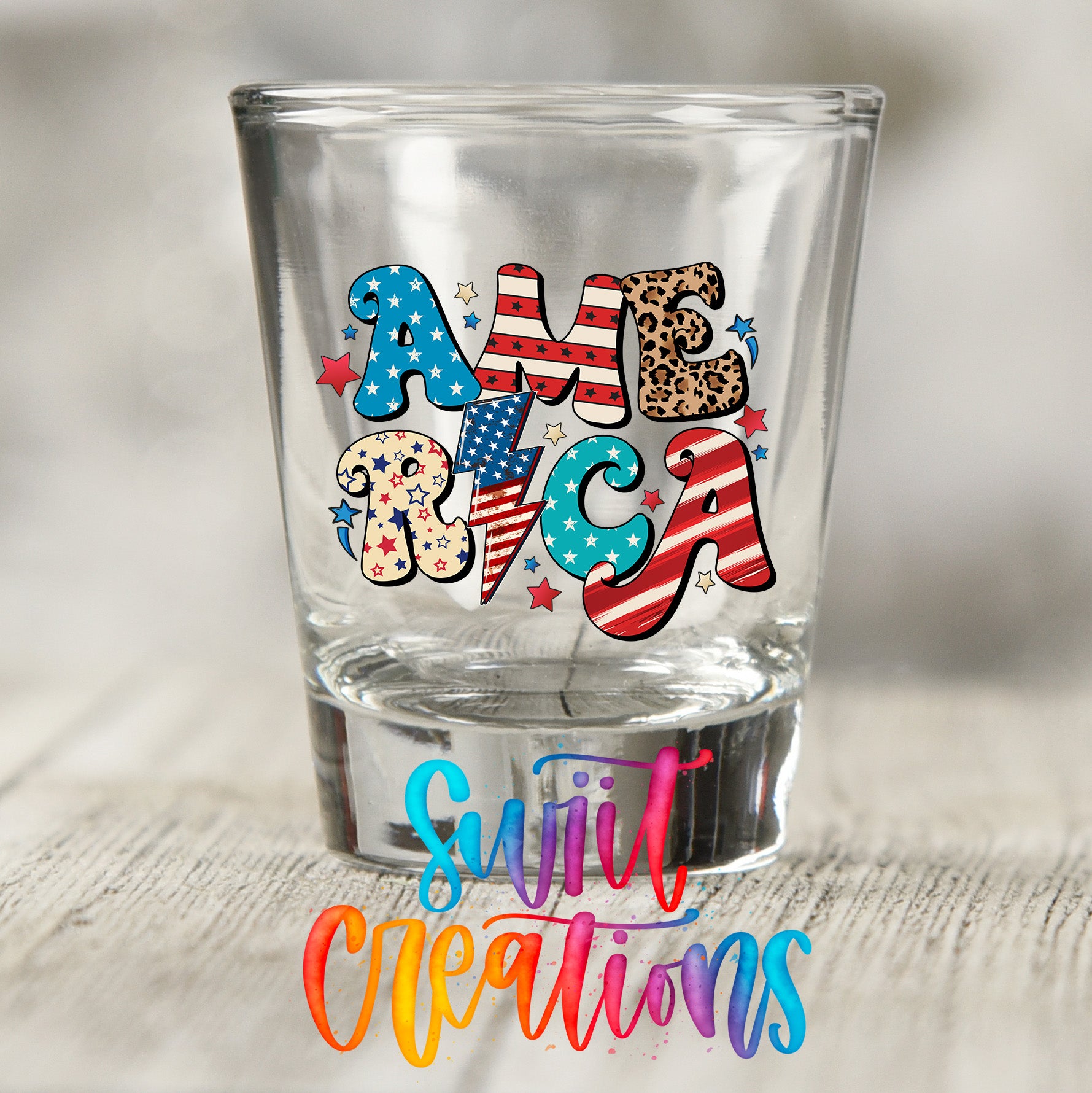 A clear glass shot glass with the word "AMERICA" printed on it in a stylized, colorful design.