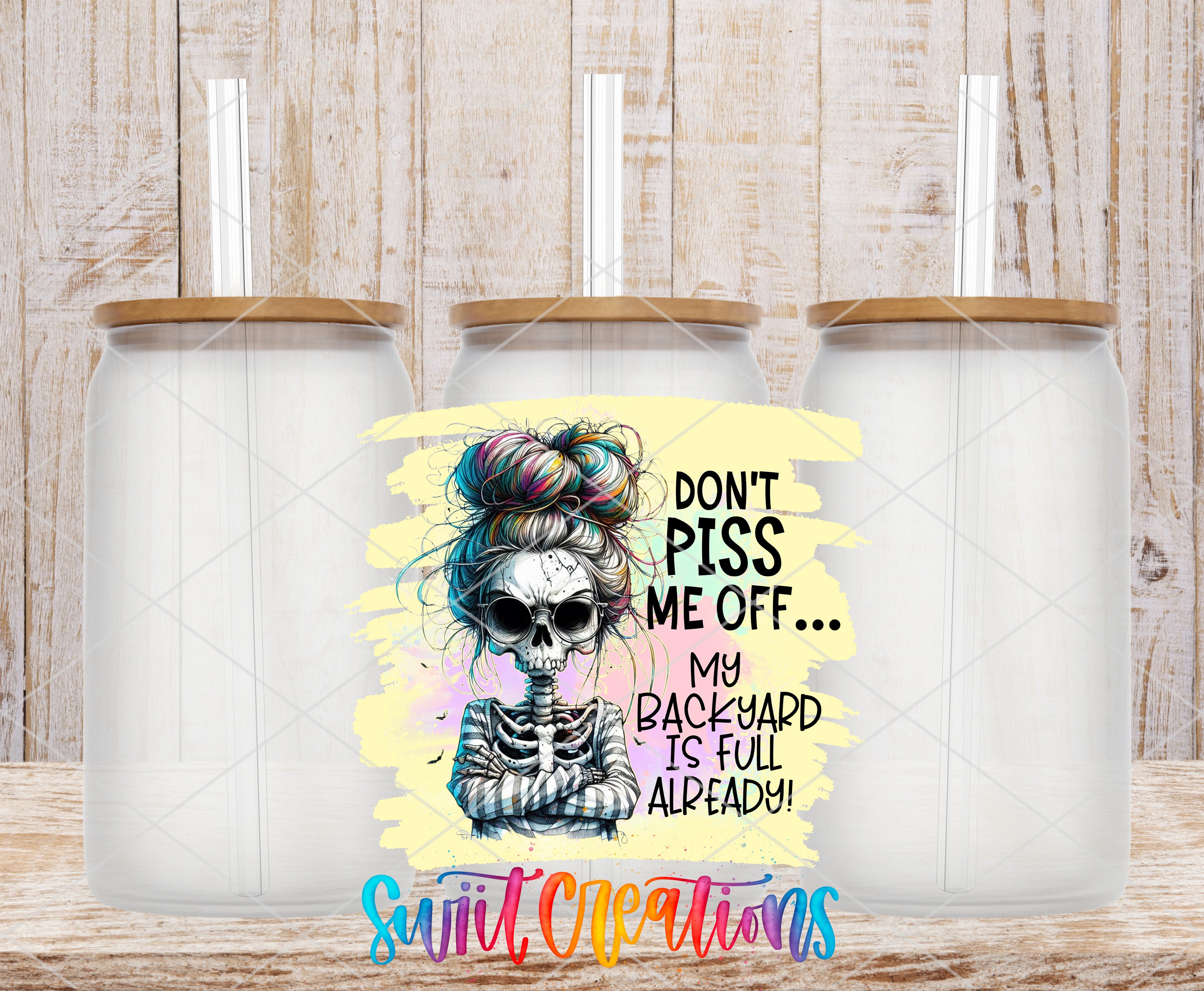a colorful illustration of a skeleton with a messy bun hairstyle, accompanied by text that reads "Don't PISS ME OFF... MY BACKYARD IS FULL ALREADY!" The image is set against a wooden background, and there are three identical clear glass jars or containers placed in front of it.