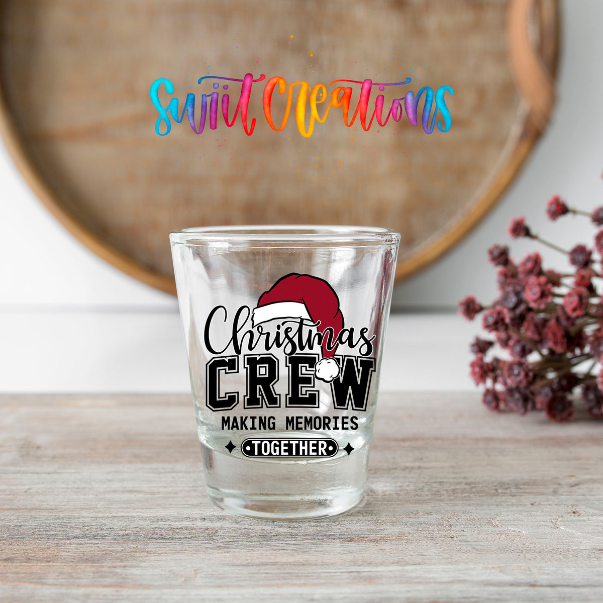 Christmas Crew Making Memories Together shot glass transfer on a clear glass beside a wooden barrel and dried flowers