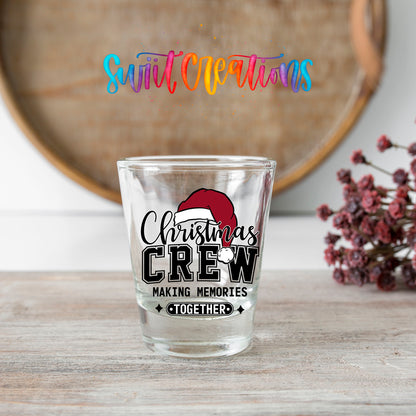 Christmas Crew Making Memories Together shot glass transfer on a clear glass beside a wooden barrel and dried flowers