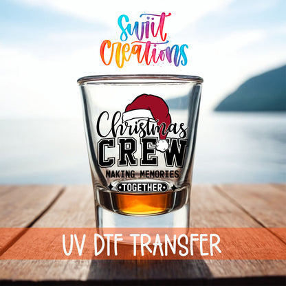 Christmas Crew Making Memories Together shot glass UV DTF transfer on a filled shot glass on a dock by the water