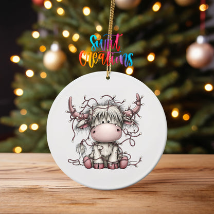 Christmas Lights Highland Cow ornament UV DTF transfer on an ornament on a wooden table with tree lights behind it