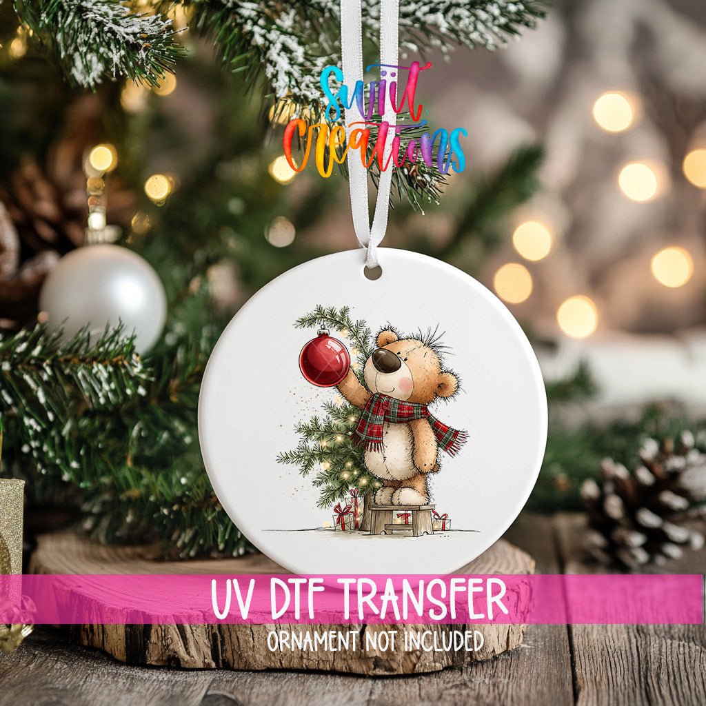 Christmas Tree Teddy Bear ornament UV DTF transfer on an ornament resting on a wood slice beside a Christmas tree