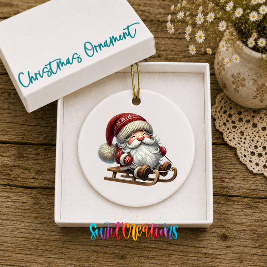Sleeping Santa on a sled ceramic Christmas ornament displayed in the included gift box