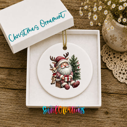 Round ceramic Christmas ornament featuring Santa with a reindeer beside a decorated Christmas tree, displayed in the included gift box