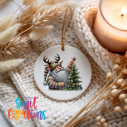 Round ceramic Christmas ornament featuring Santa placing a star on a Christmas tree, styled beside a candle and cozy knit blanket