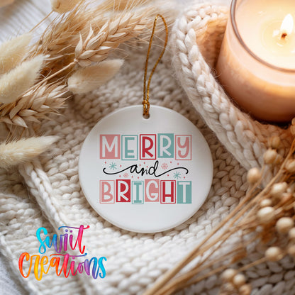 Round ceramic Christmas ornament featuring pastel block-letter Merry and Bright holiday typography, styled beside a candle and cozy knit blanket
