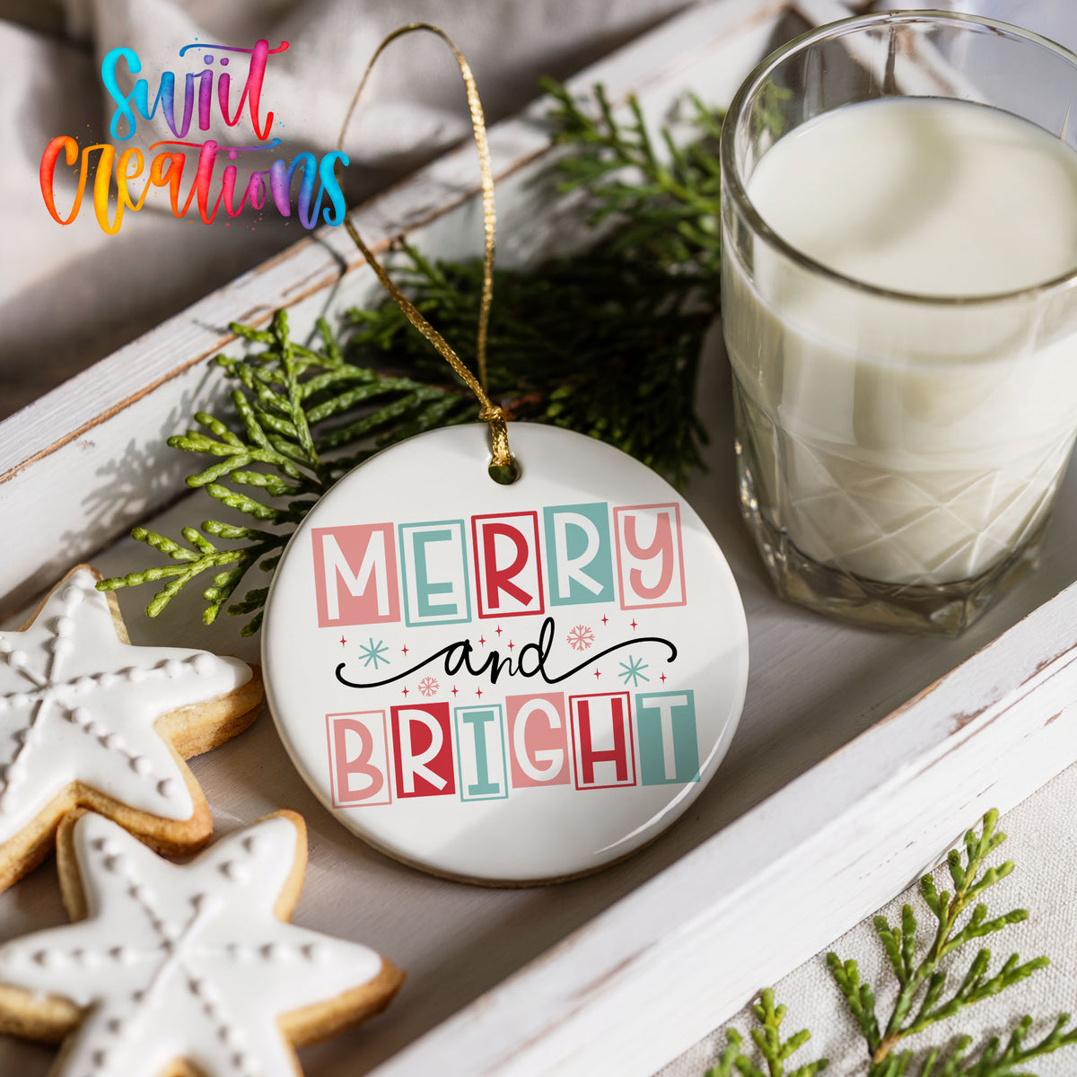 Round ceramic Christmas ornament featuring pastel block-letter Merry and Bright holiday typography, styled with cookies and milk