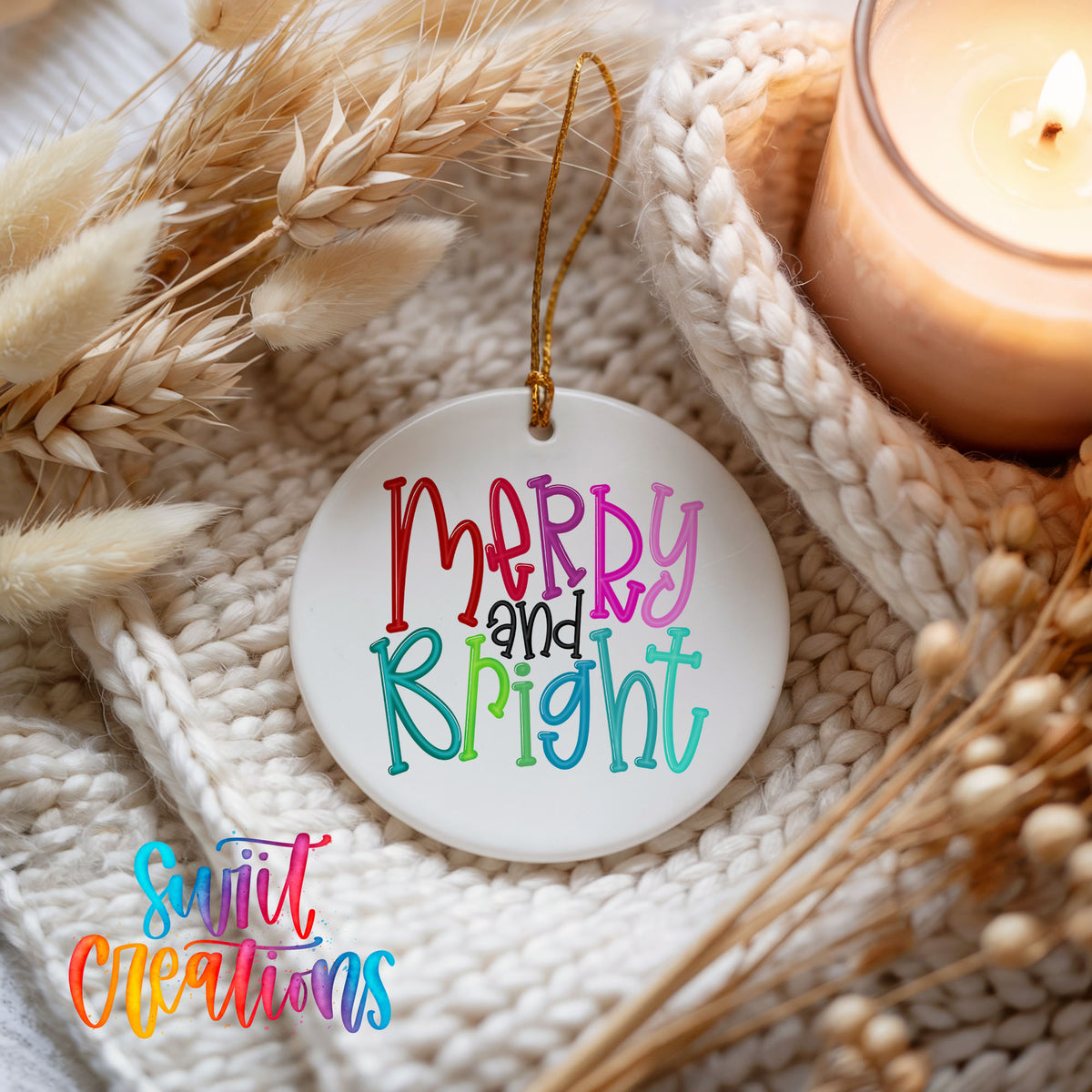 Round ceramic Christmas ornament featuring colorful hand-lettered Merry and Bright holiday typography, styled beside a candle and cozy knit blanket