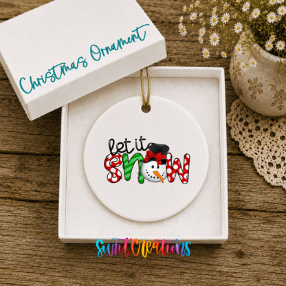 Round ceramic Christmas ornament featuring playful red and black Let It Snow holiday typography, displayed in the included gift box