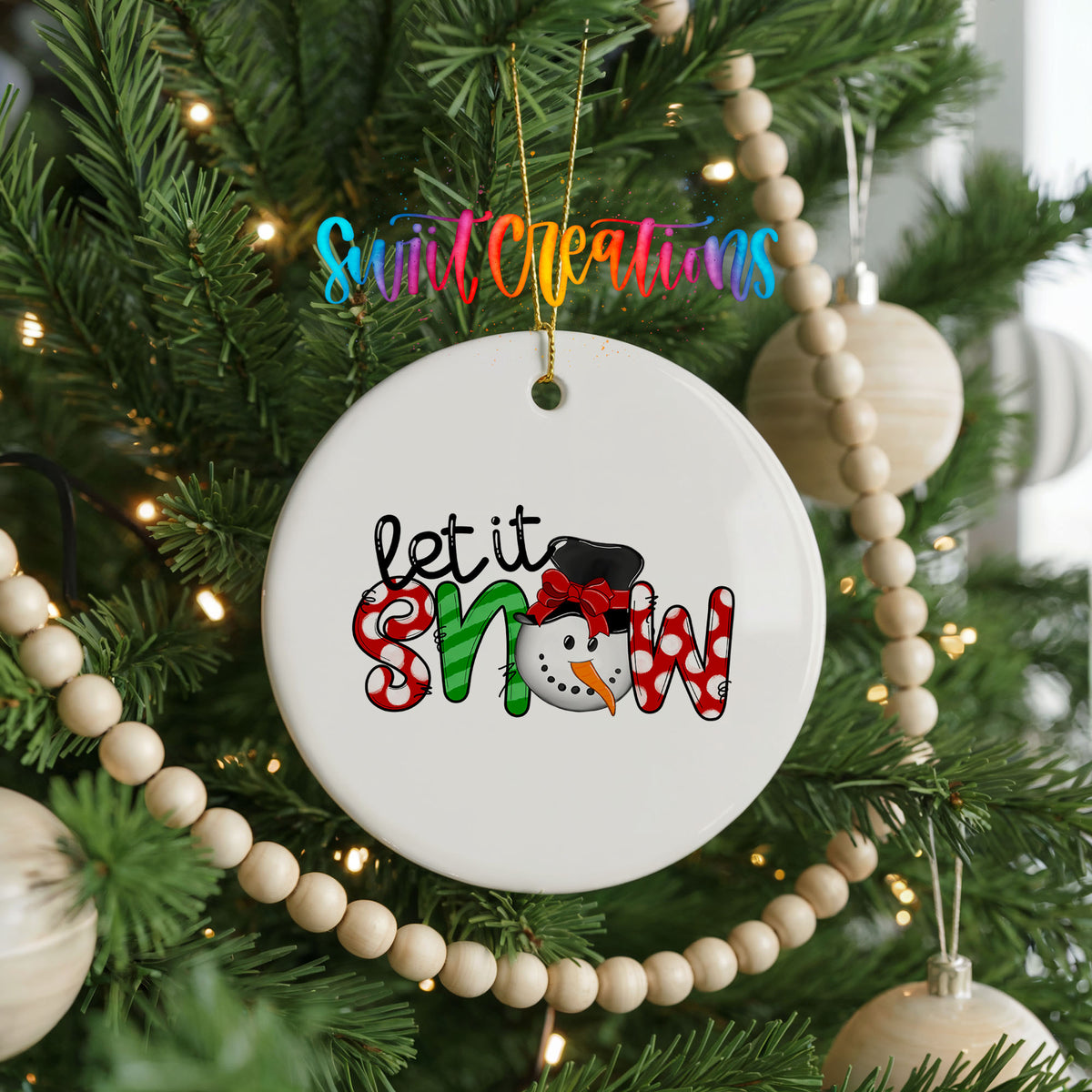 Round ceramic Christmas ornament featuring playful red and black Let It Snow holiday typography, hanging on a decorated Christmas tree
