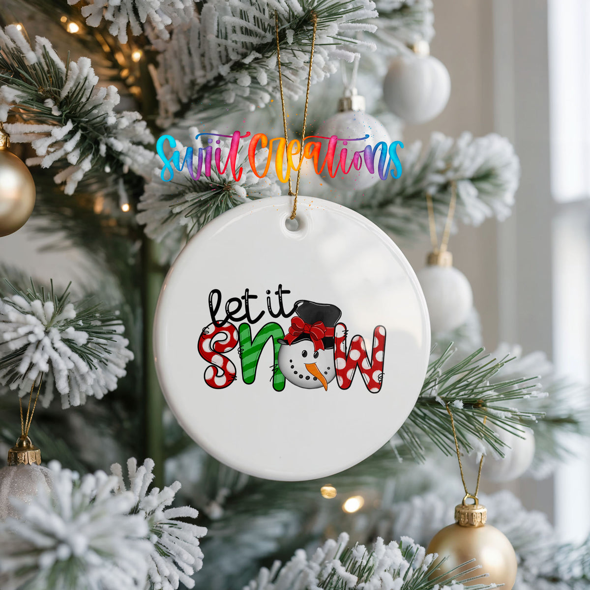 Round ceramic Christmas ornament featuring playful red and black Let It Snow holiday typography, hanging on a frosted Christmas tree