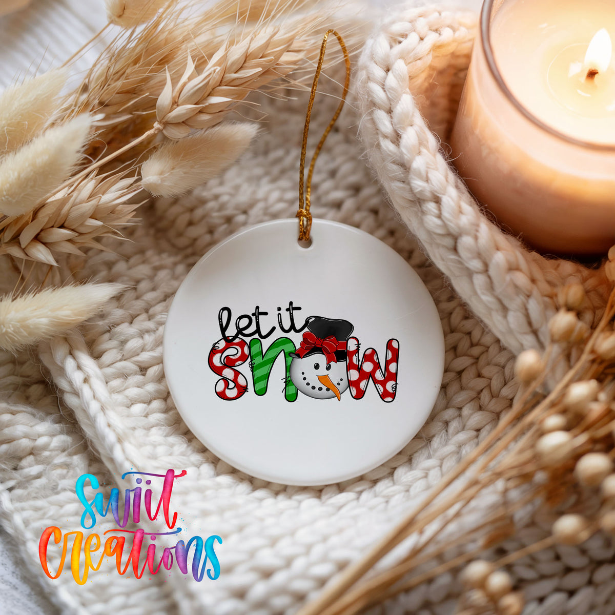 Round ceramic Christmas ornament featuring playful red and black Let It Snow holiday typography, styled beside a candle and cozy knit blanket