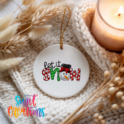 Round ceramic Christmas ornament featuring playful red and black Let It Snow holiday typography, styled beside a candle and cozy knit blanket