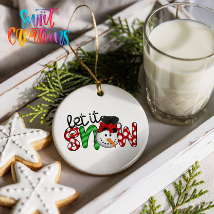Round ceramic Christmas ornament featuring playful red and black Let It Snow holiday typography, styled with cookies and milk
