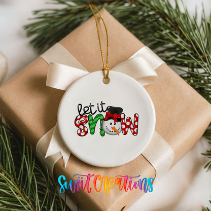 Round ceramic Christmas ornament featuring playful red and black Let It Snow holiday typography, placed on a wrapped Christmas gift