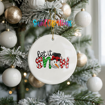 Round ceramic Christmas ornament featuring playful red and black Let It Snow holiday typography, hanging on a frosted holiday tree