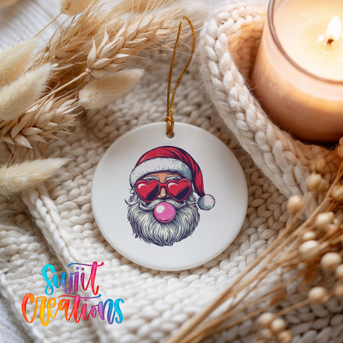 Round ceramic Christmas ornament featuring retro Santa wearing sunglasses and blowing pink bubblegum, styled beside a candle and cozy knit blanket