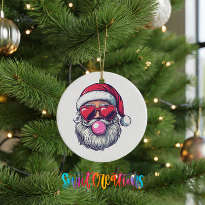 Round ceramic Christmas ornament featuring retro Santa wearing sunglasses and blowing pink bubblegum, hanging on a green Christmas tree