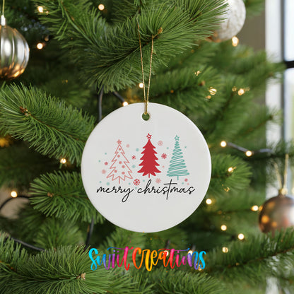 Round ceramic Christmas ornament featuring minimalist red and mint Christmas trees with Merry Christmas script, hanging on a green Christmas tree