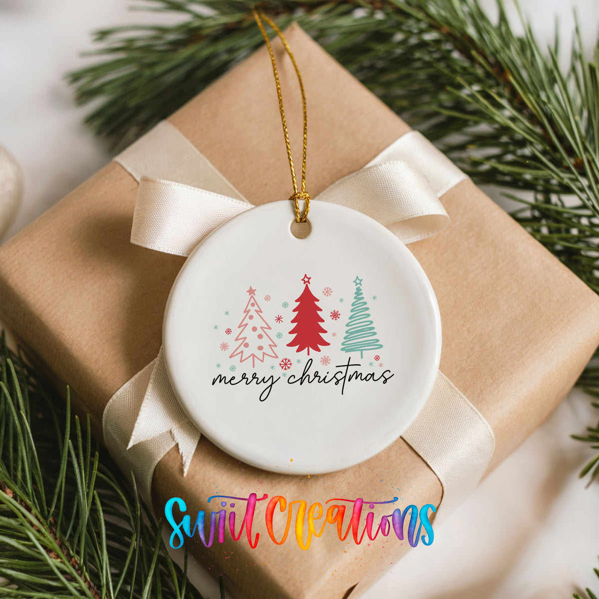 Round ceramic Christmas ornament featuring minimalist red and mint Christmas trees with Merry Christmas script, placed on a wrapped Christmas gift
