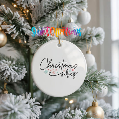 Round ceramic Christmas ornament featuring delicate Christmas Vibes script with small colorful holiday accents, hanging on a frosted Christmas tree