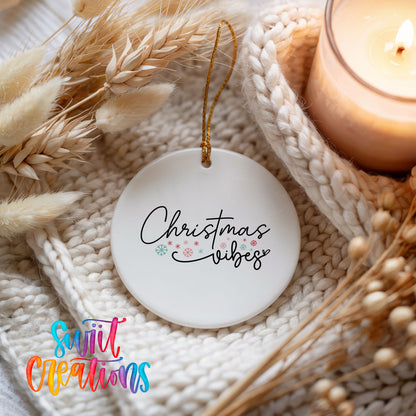 Round ceramic Christmas ornament featuring delicate Christmas Vibes script with small colorful holiday accents, styled beside a candle and cozy knit blanket