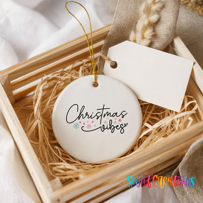 Round ceramic Christmas ornament featuring delicate Christmas Vibes script with small colorful holiday accents, presented in a rustic wooden gift crate