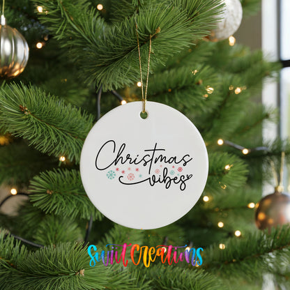 Round ceramic Christmas ornament featuring delicate Christmas Vibes script with small colorful holiday accents, hanging on a green Christmas tree
