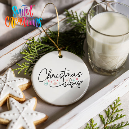 Round ceramic Christmas ornament featuring delicate Christmas Vibes script with small colorful holiday accents, styled with cookies and milk