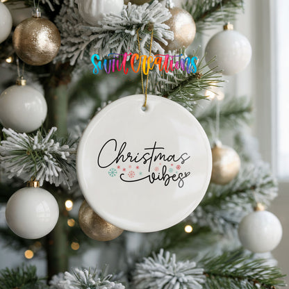 Round ceramic Christmas ornament featuring delicate Christmas Vibes script with small colorful holiday accents, hanging on a frosted holiday tree