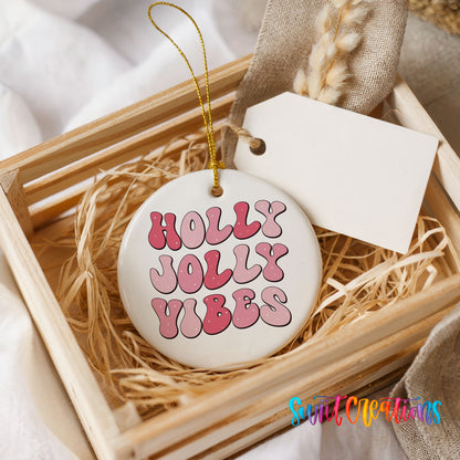 Round ceramic Christmas ornament featuring pink retro Holly Jolly Vibes typography, presented in a rustic wooden gift crate