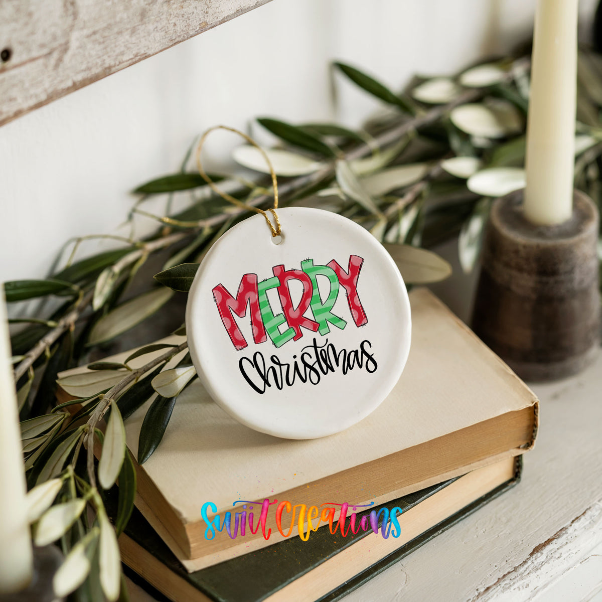 Round ceramic Christmas ornament featuring colorful patterned Merry Christmas typography, styled on books with holiday greenery