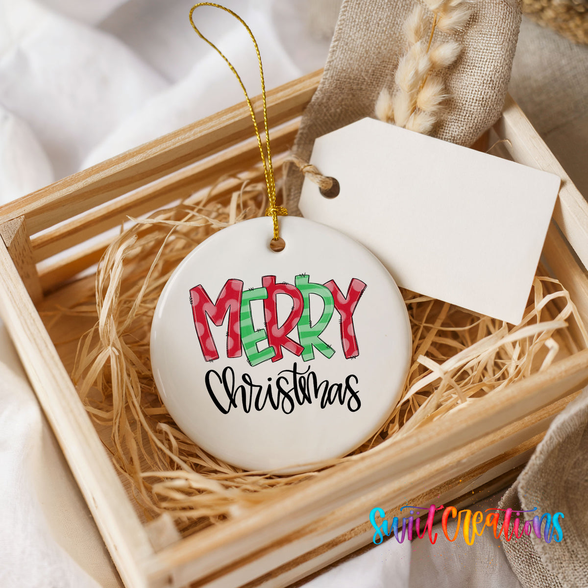 Round ceramic Christmas ornament featuring colorful patterned Merry Christmas typography, presented in a rustic wooden gift crate